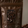 Matte brown stand-up chocolate packaging pouch with a clear window showing chocolate chunks, cocoa beans beside it