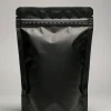 Matte black stand-up pouch with tamper-evident tear band and press-to-close zipper on a light grey studio background
