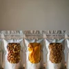 Row of matte resealable stand-up pouches filled with coffee, nuts, dried fruit and granola on a wooden table, illustrating food packaging shelf life