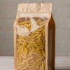 Kraft-front stand-up pasta packaging bag with a clear window and zipper, filled with dried penne on a wooden table