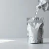 an unbranded stand-up spout pouch with a screw cap, tilted in mid-pour with a clear liquid stream, clean studio background